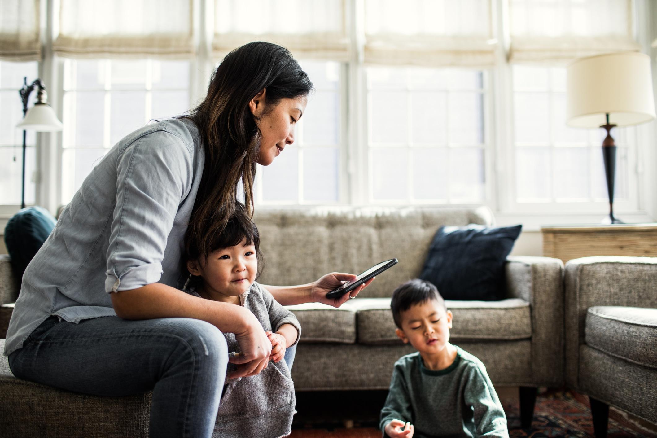 Une femme assise avec ses deux enfants et souriant devant un téléphone intelligent.