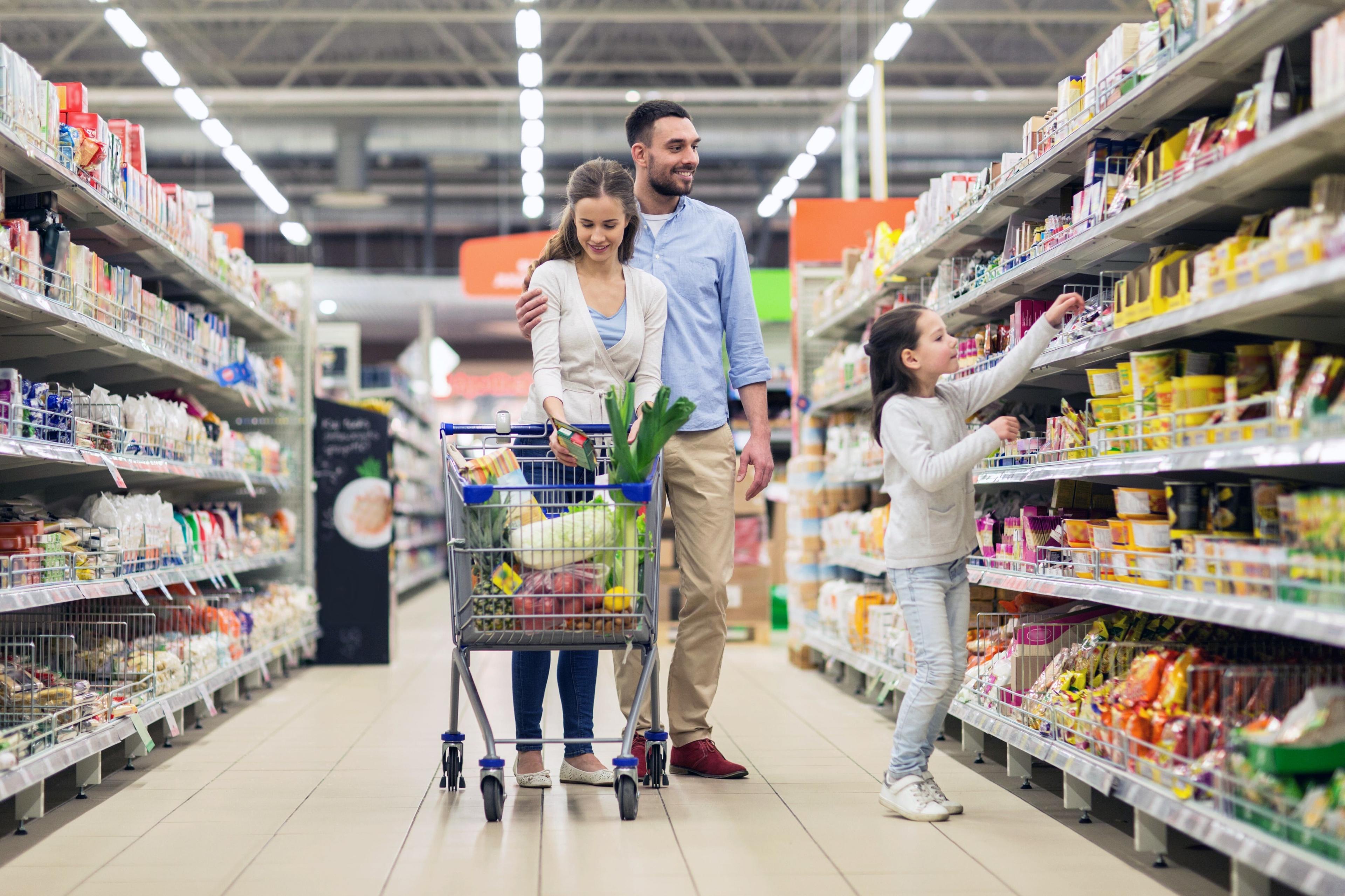 Une famille pousse un chariot dans l'allée d'une épicerie.